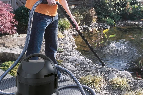 Person reinigt Teich mit Schlammsauger